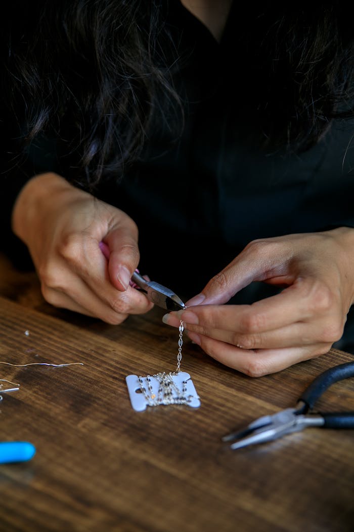 contact-img Focused shot of handmade jewelry making with pliers and beads on a wooden table.