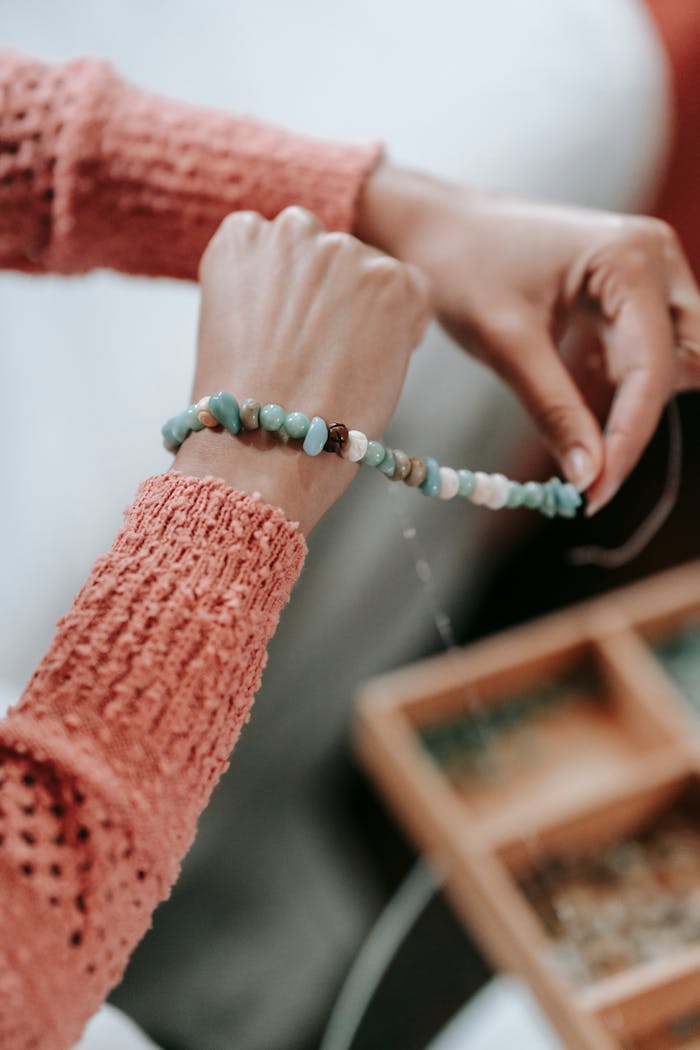 A woman creates a handmade bracelet with colorful beads, showcasing her craft in a cozy indoor setting.